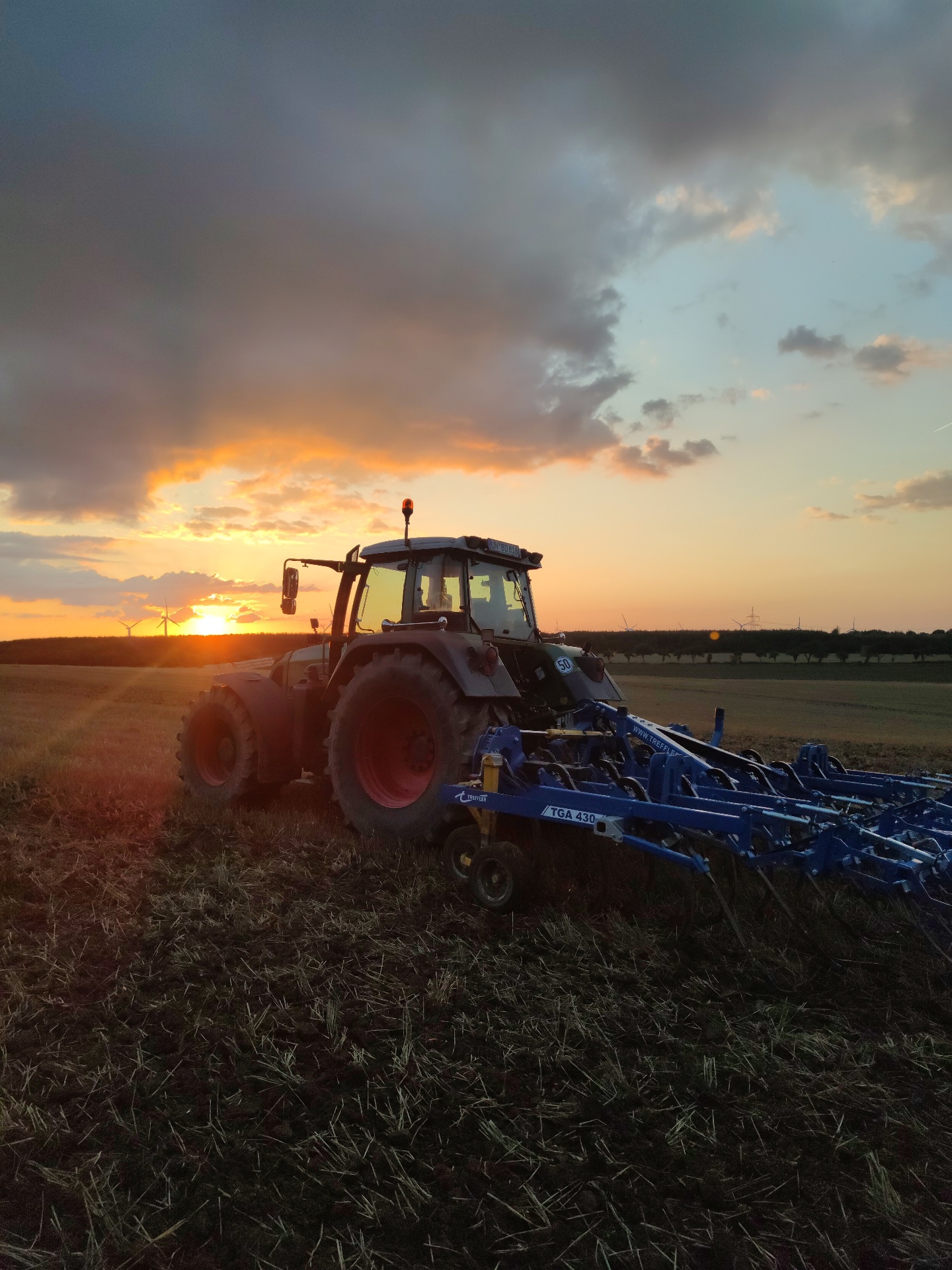 Traktor mit Grubber bei Sonnenuntergang