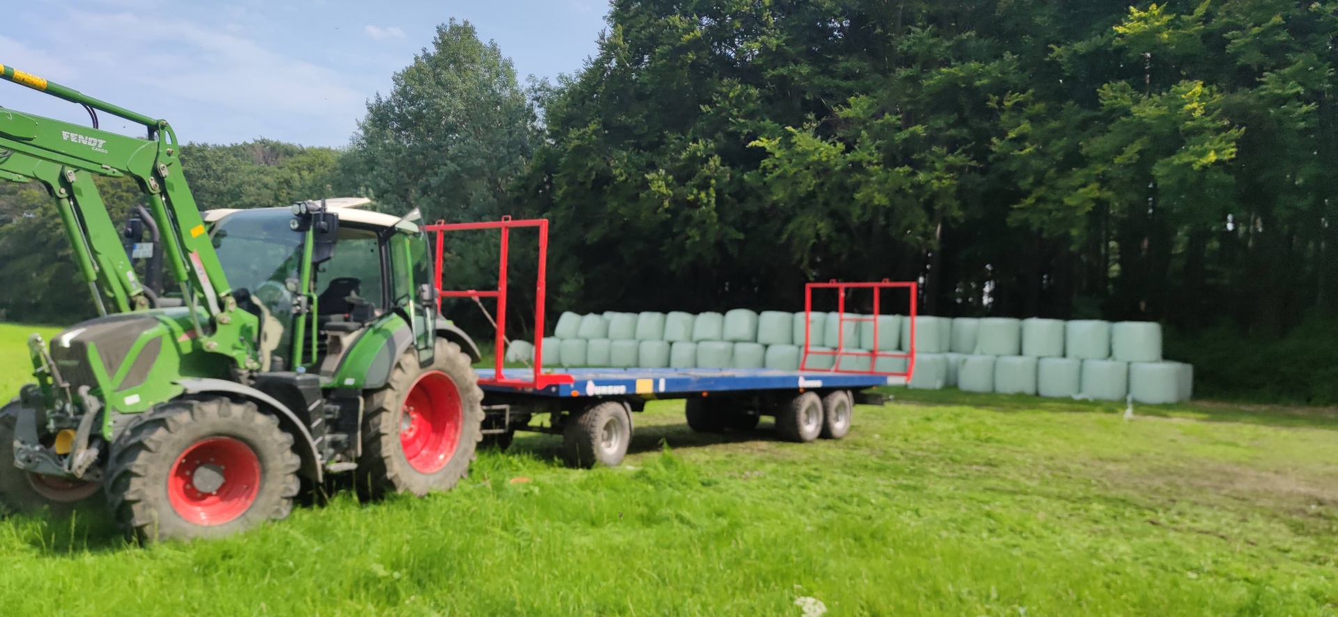 Fendt Traktor mit Ballenanhänger vor gestapelten Silageballen
